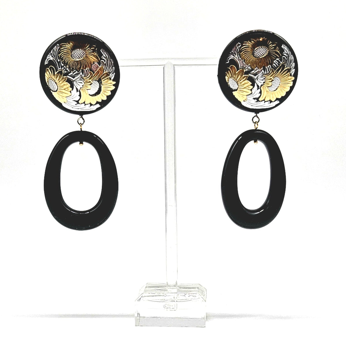 Pair of earrings with floral design and black oval shapes on a clear stand.