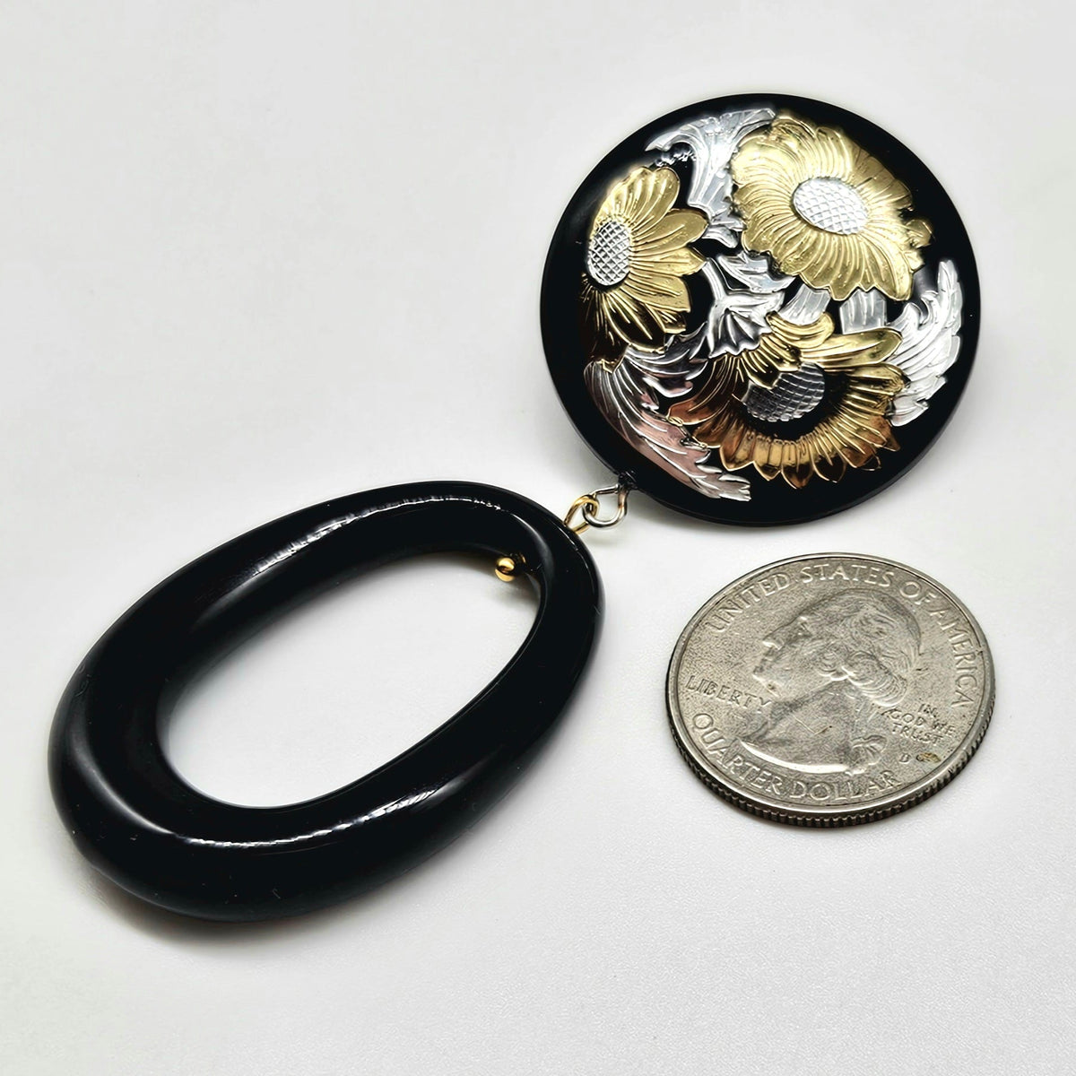 Black and gold floral earrings with a quarter for scale on a white background