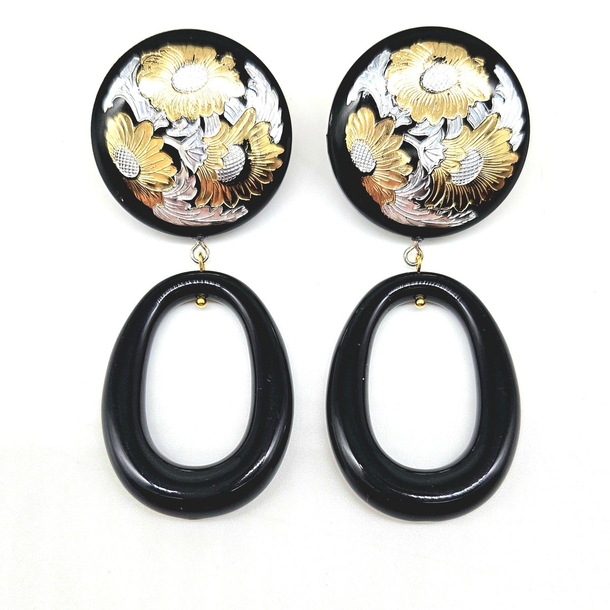 Pair of earrings with black oval drops and floral designs in gold and silver on a white background
