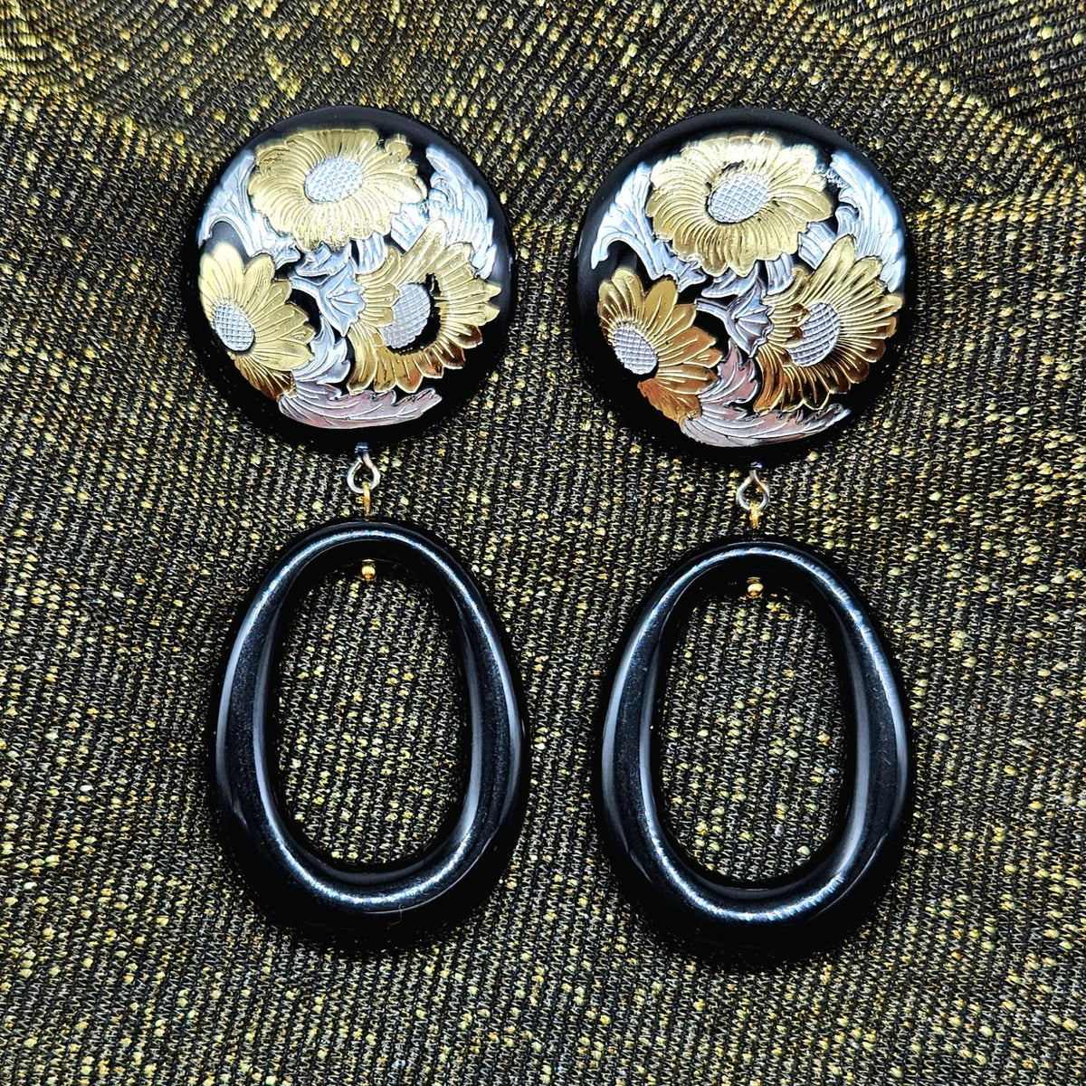 Pair of earrings with floral designs on a textured fabric background