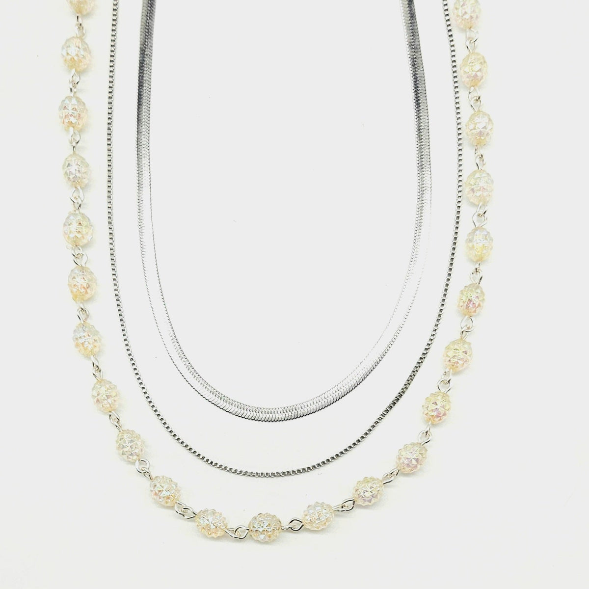 Three-strand silver chain and lucite beaded necklace on a white background