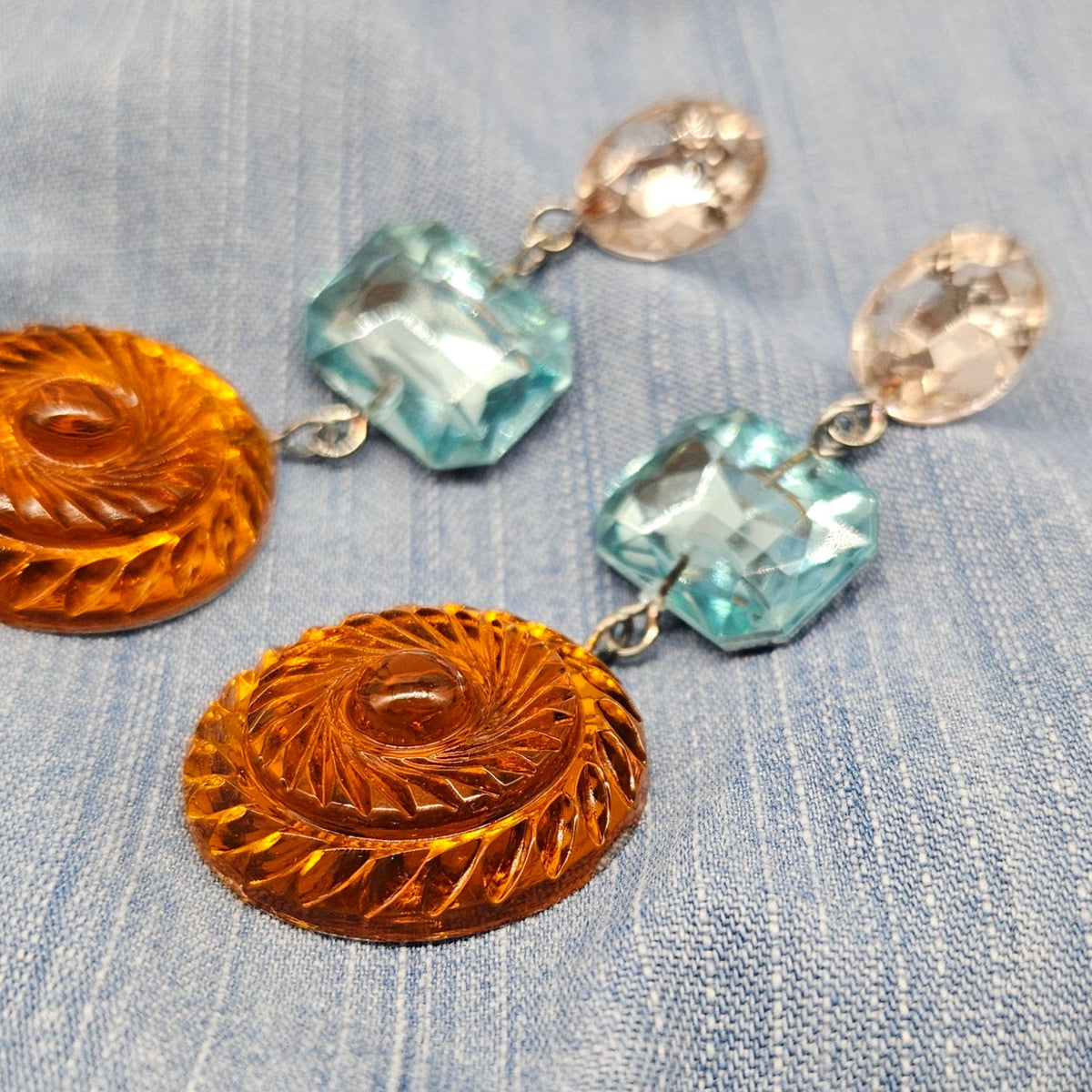 Pair of earrings with orange and blue gemstones on a denim background