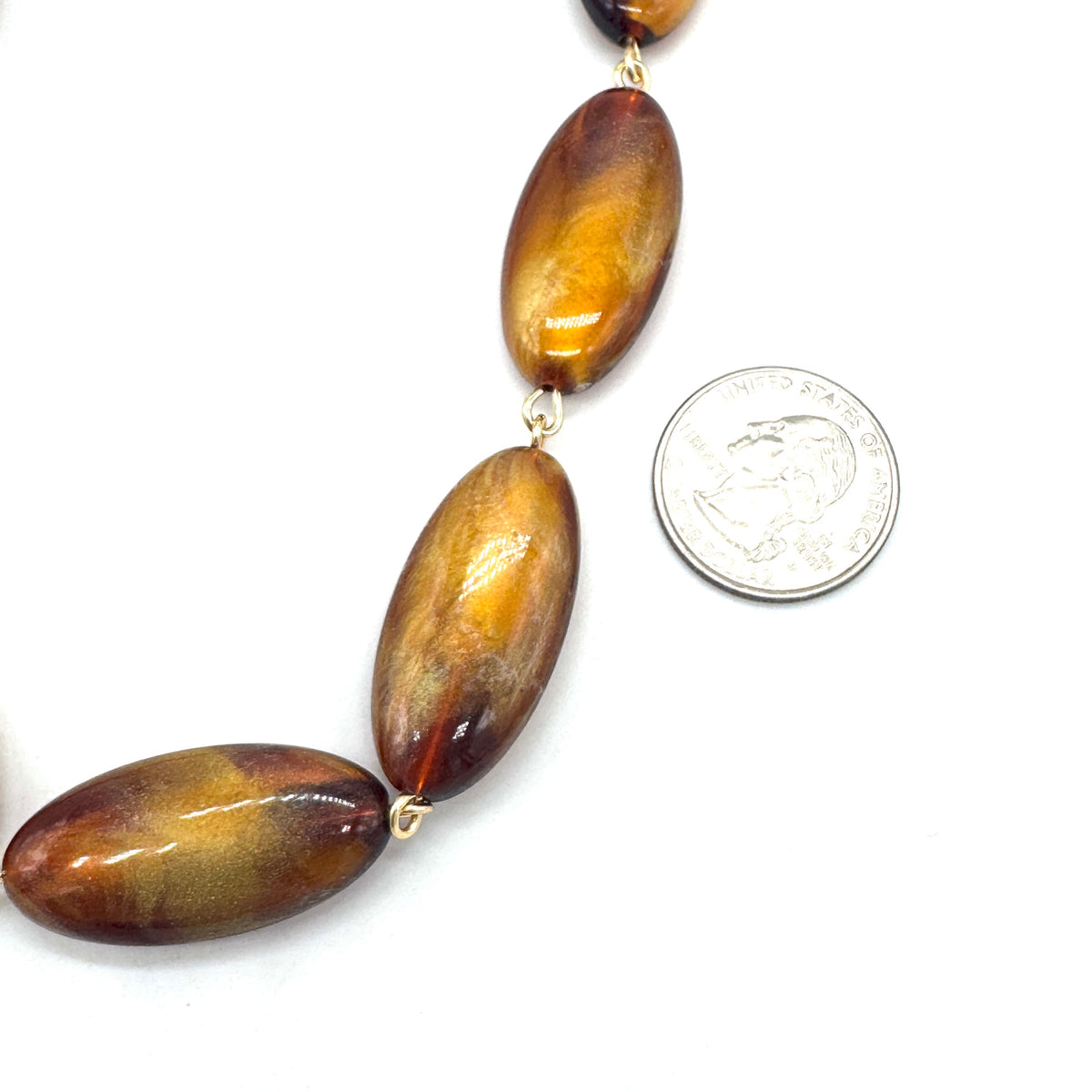 Necklace with large brown beads next to a quarter for scale on a white background