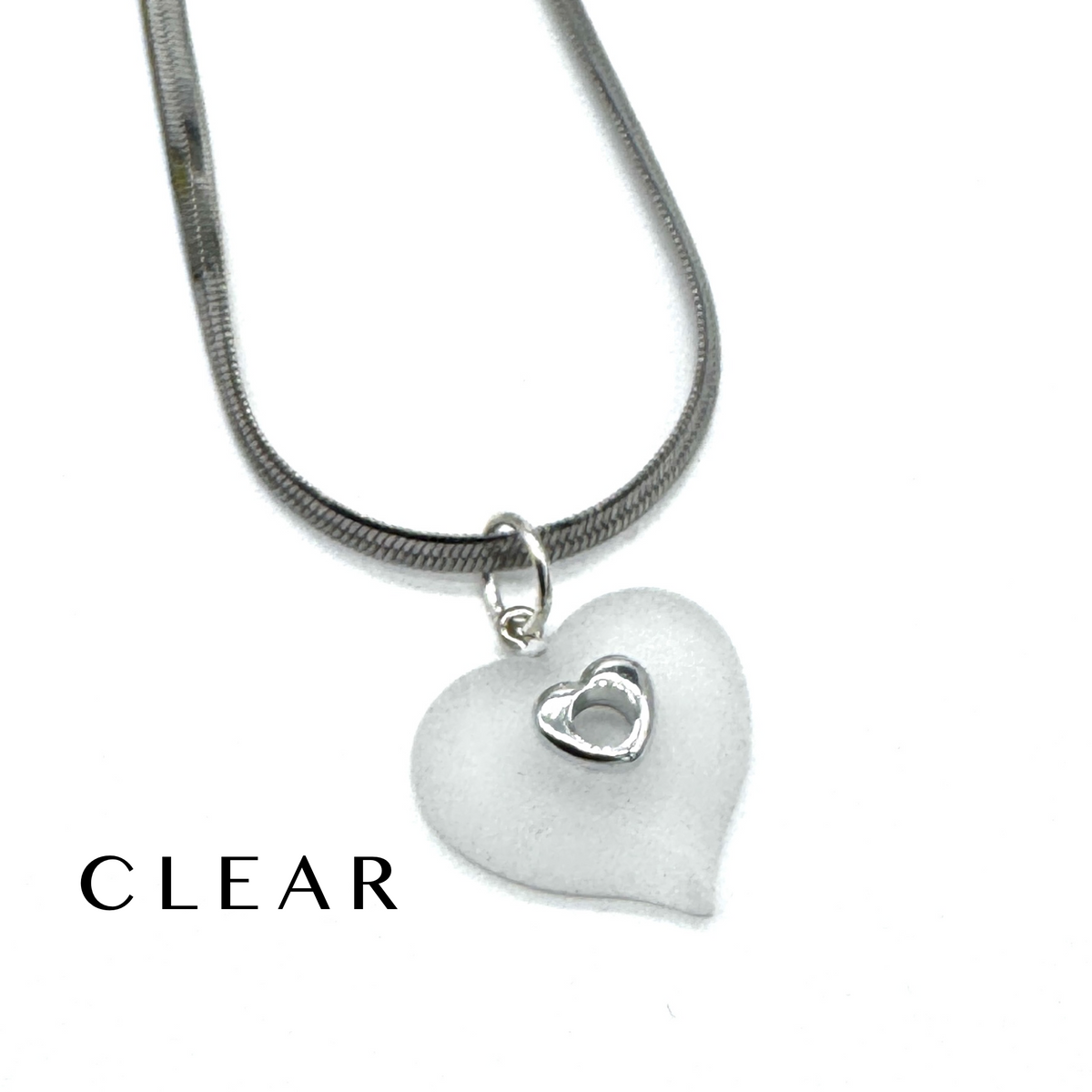 A silver snake chain necklace with a frosted clear heart-shaped pendant featuring a small silver heart in the center, shown on a white background with the word 'CLEAR' printed in the lower left.