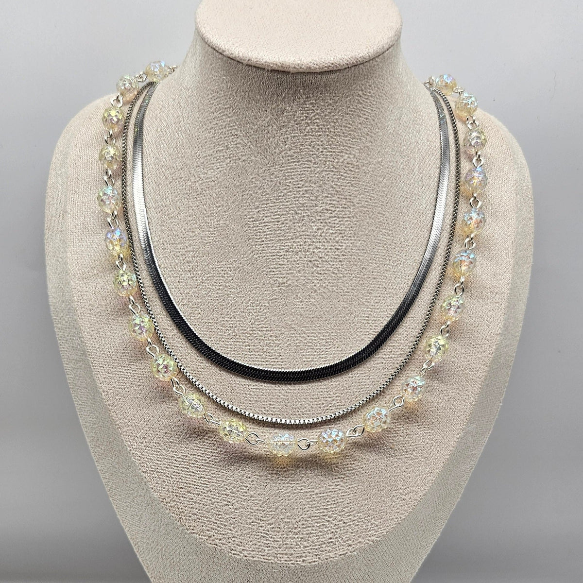 Silver necklace with multiple strands on a mannequin bust against a gray background