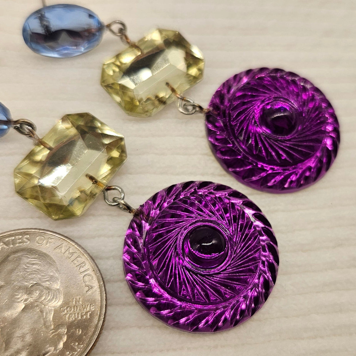 Purple and yellow earrings on a light wooden surface with a quarter for scale.