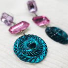 Earrings with a blue circular pendant and pink and purple gemstones on a white background