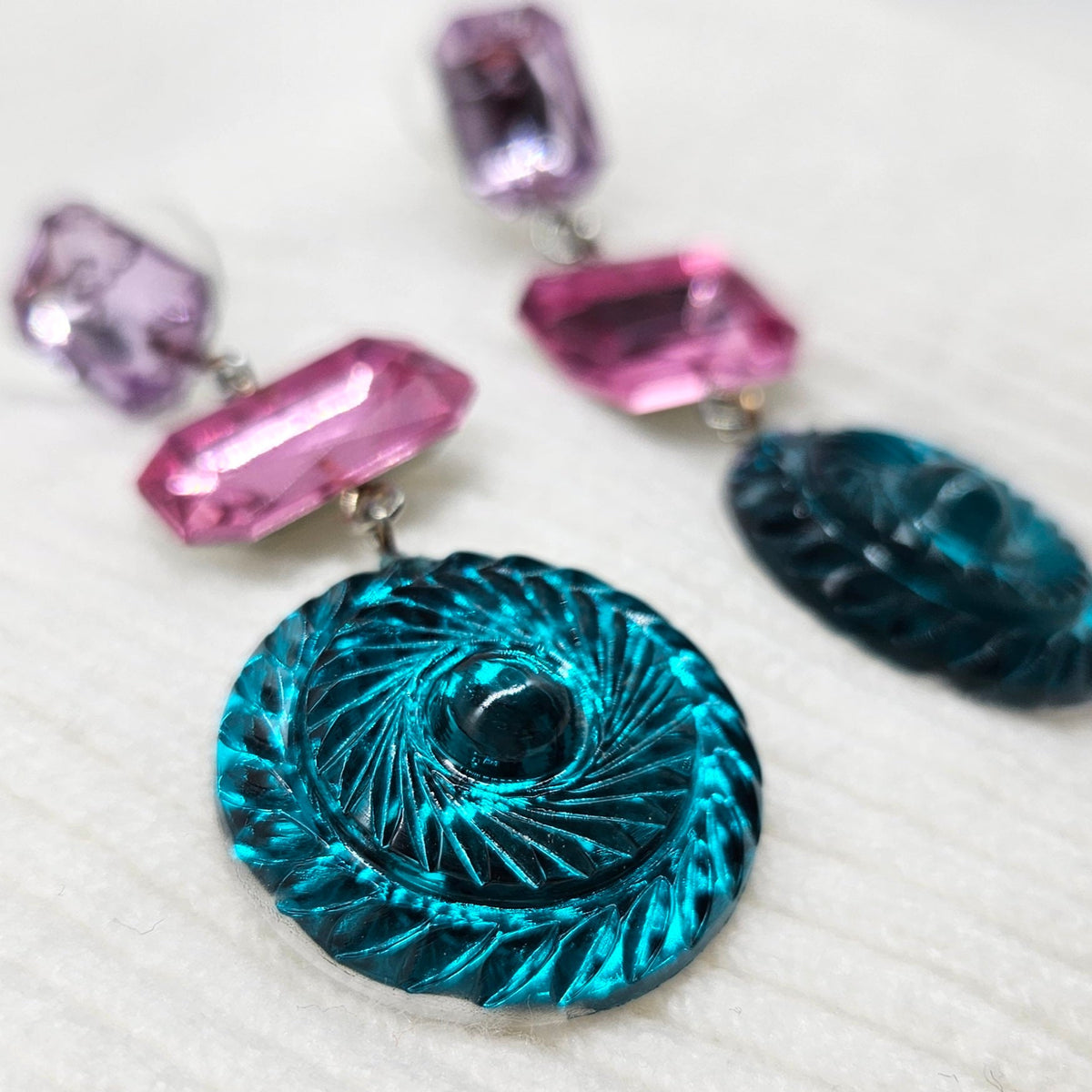 Earrings with a blue circular pendant and pink and purple gemstones on a white background