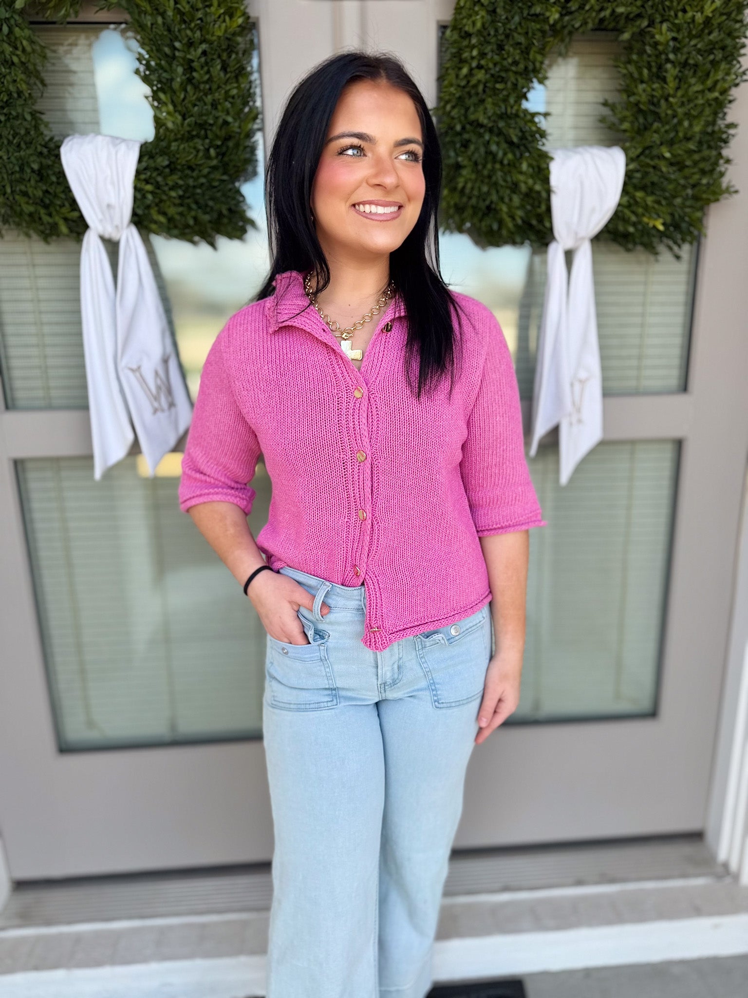 Woman wearing a pink shirt and light blue jeans standing in front of a door with wreaths and bows.