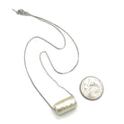 Silver necklace with a cylindrical pendant next to a quarter for scale on a white background