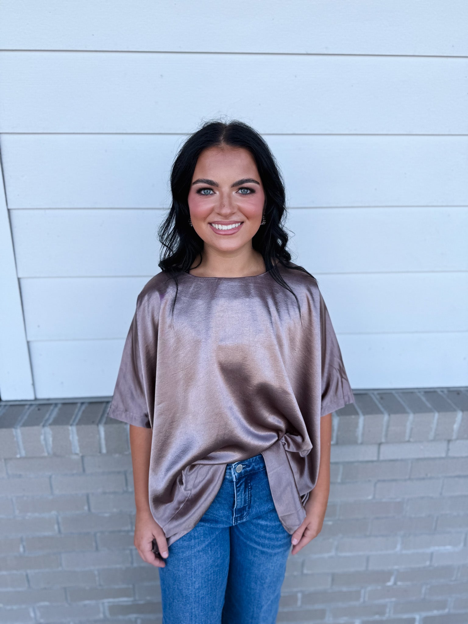 Woman wearing a brown oversized shirt and blue jeans standing against a light blue wall.