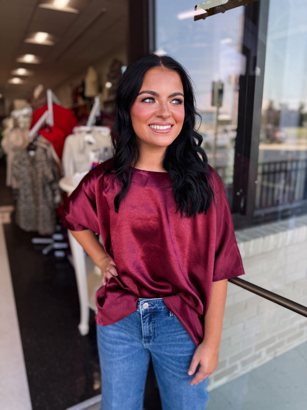Woman wearing a burgundy top and blue jeans standing in front of a store with mannequins.