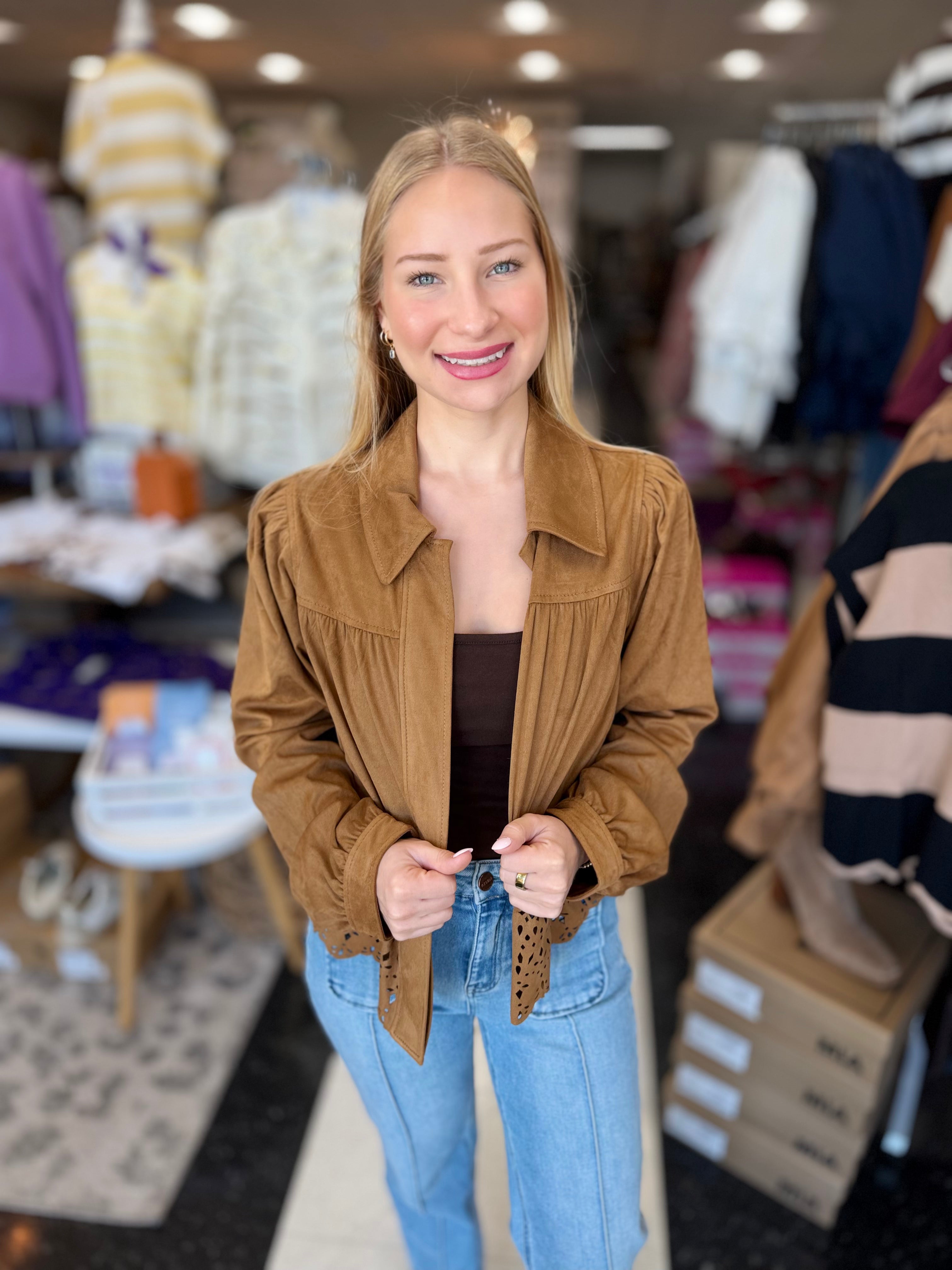 A woman wearing a brown corduroy jacket over a black top and light blue jeans, standing inside a clothing store.